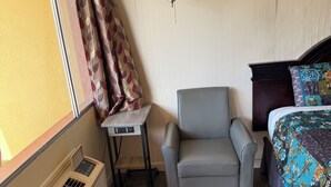 A bedroom with a bed, a chair, a table, a heater, and a window with curtains. - Down Towner Inn (Grangeville)