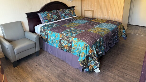 A neatly arranged bedroom with a large bed, a chair, and a wooden headboard. - Down Towner Inn (Grangeville)