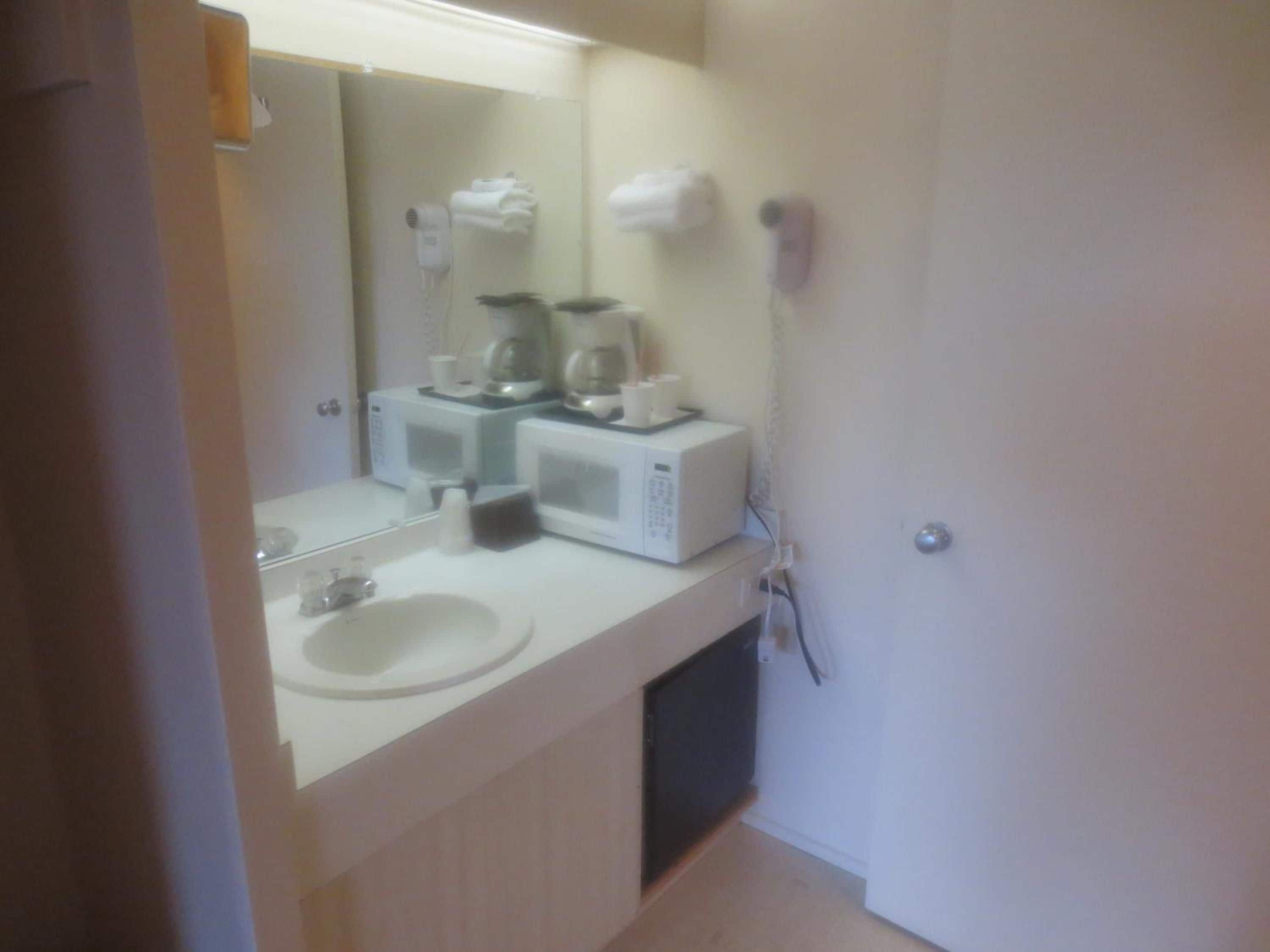 Un baño con un lavabo blanco, un espejo y dos microondas blancas sobre la encimera.