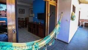 A room with a hammock, wooden door, and a TV in the background. - Pousada do Frade (Ipojuca)