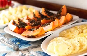 A table with plates of sliced fruits, including papaya and pineapple. - Pousada do Frade (Ipojuca)