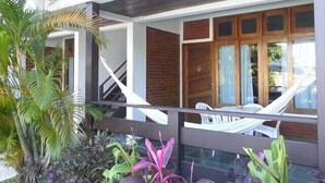 A modern building with a covered outdoor area, featuring a staircase, wooden doors, and a seating area with white chairs. - Pousada do Frade (Ipojuca)