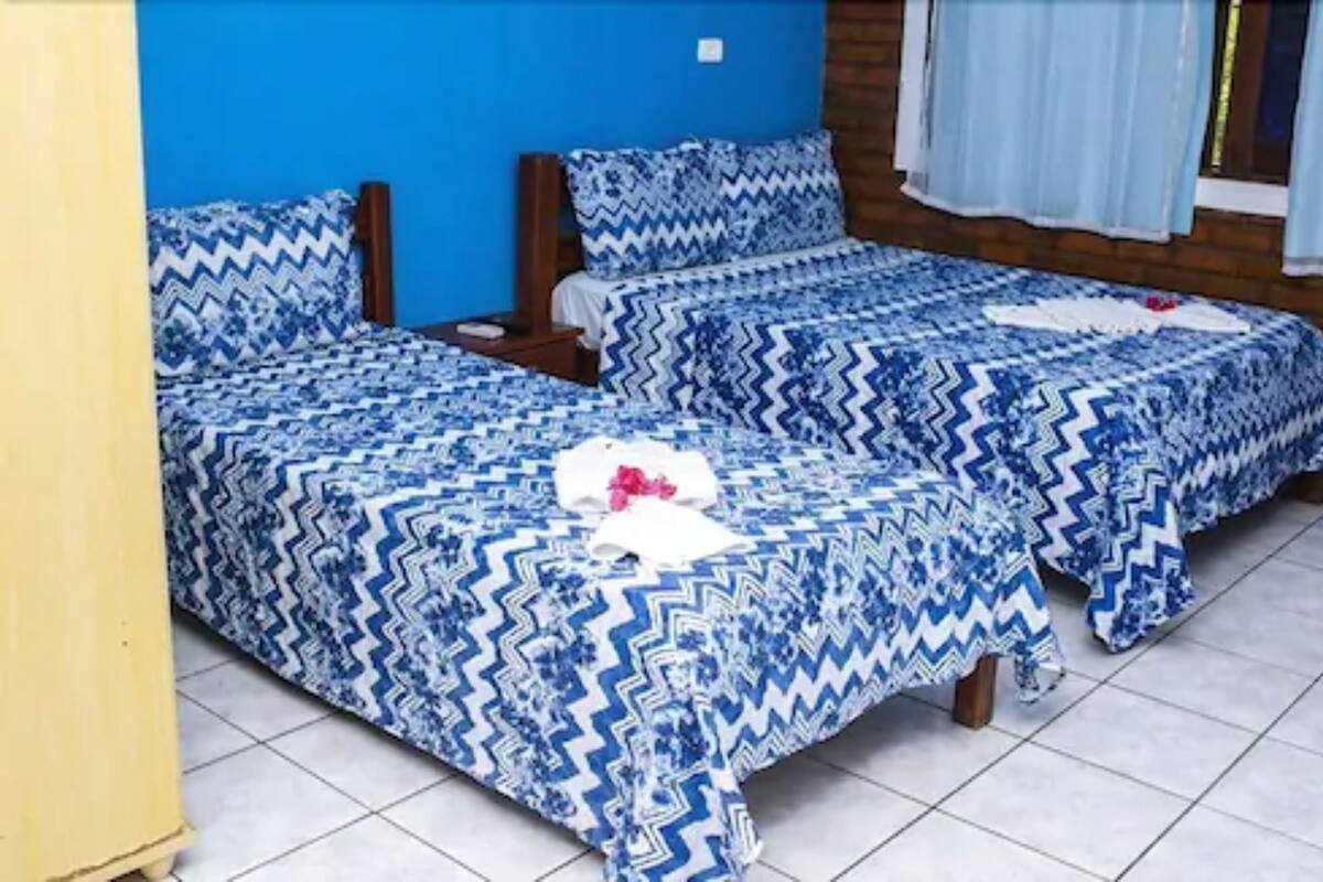 Une chambre avec deux lits, chacun agrémenté de draps à motifs bleus, de têtes de lit en bois et d’une fenêtre ornée de rideaux bleu clair.