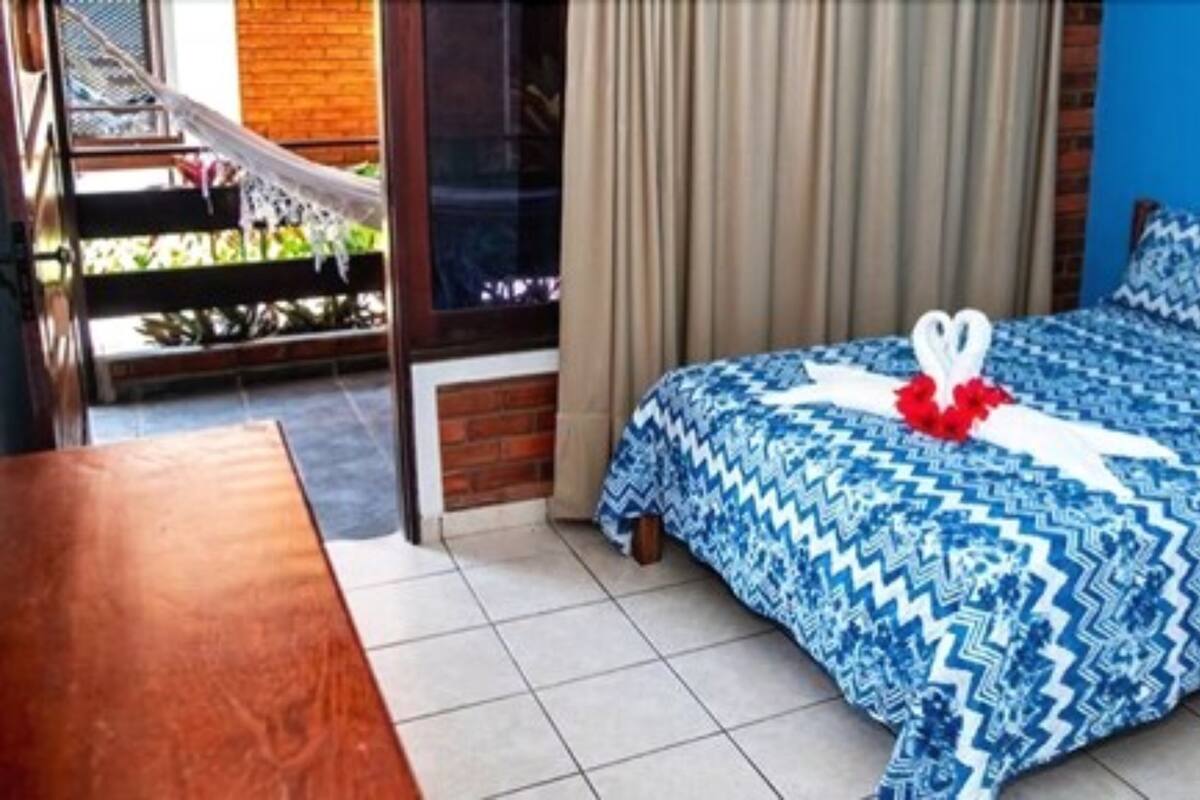 Une chambre d’hôtel avec un lit, une table en bois, un hamac et une vue sur l’extérieur.