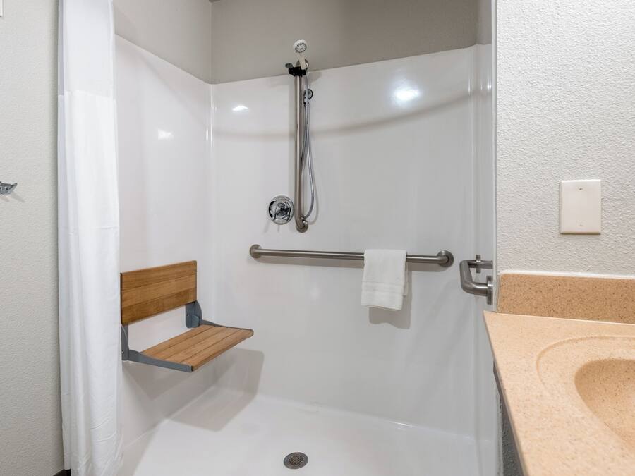 A shower with a handheld showerhead, a towel rack, and a wooden shelf.