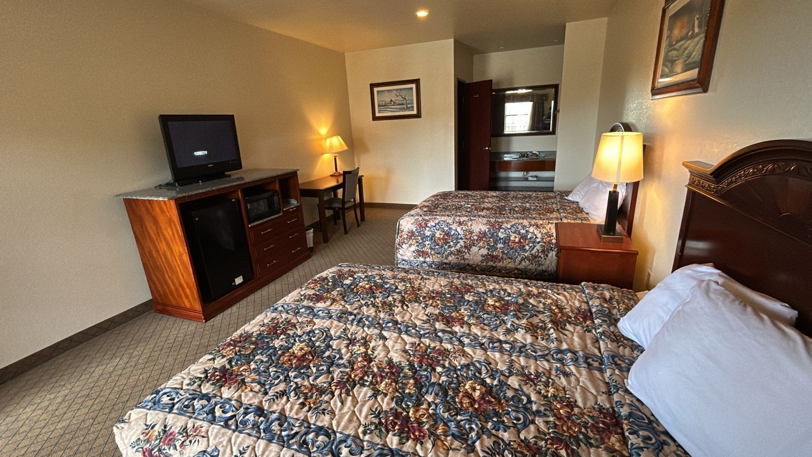 Habitación de hotel con dos camas, televisor, escritorio y una silla.