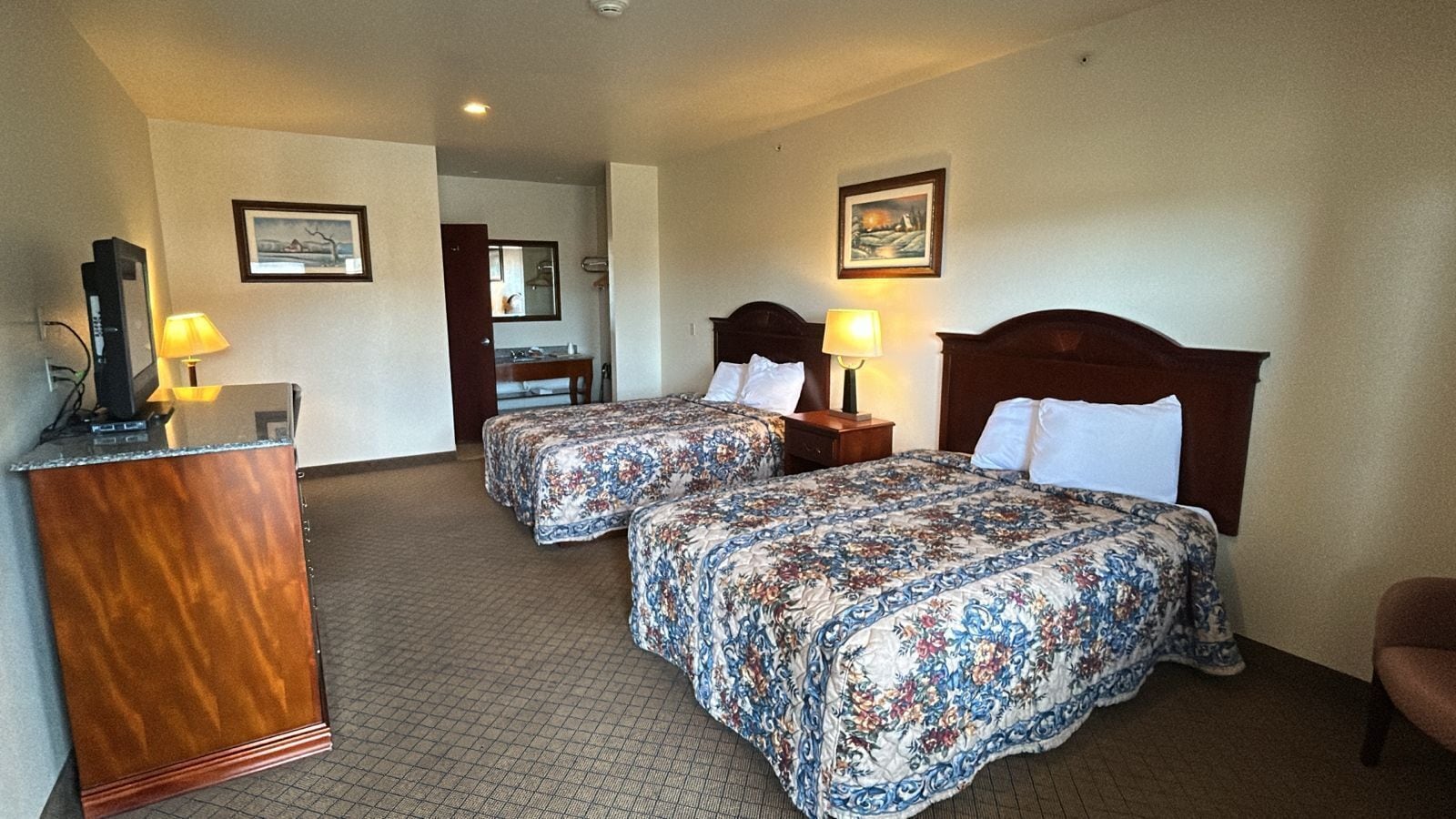 Ein Hotelzimmer mit zwei Betten, einem Schreibtisch, einem Spiegel und einem durchgegangenen Badezimmer.