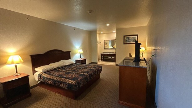 Habitación de hotel con cama doble, escritorio, silla, espejo y baño con lavamanos y espejo.