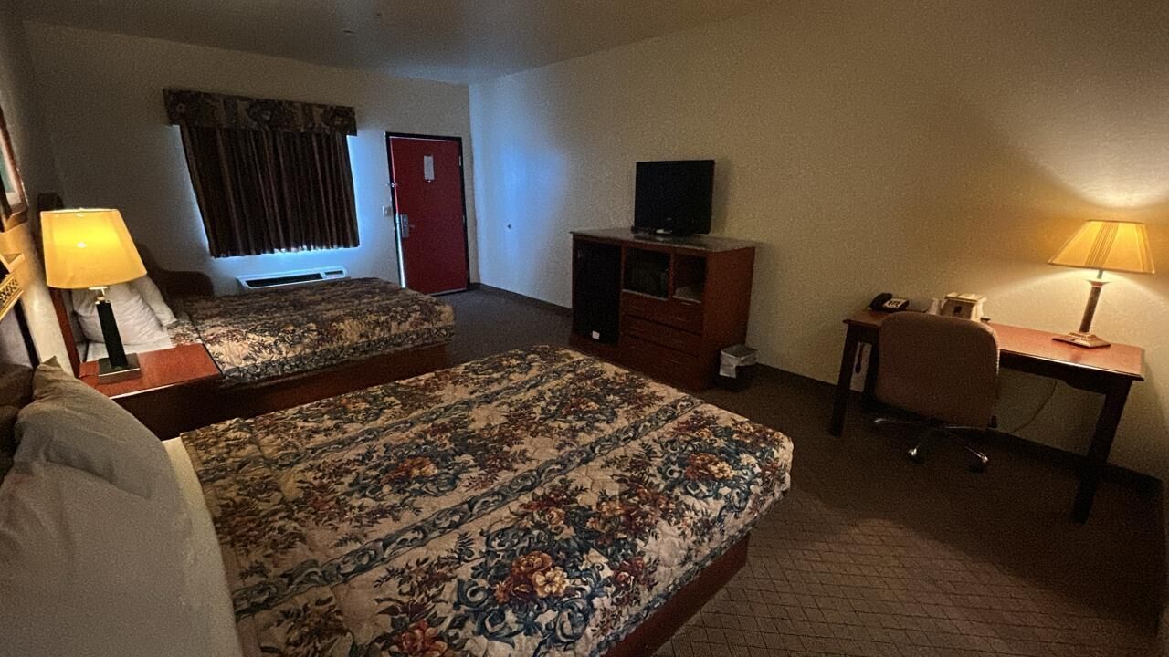 Una habitación de hotel con dos camas, un escritorio, una silla, un televisor y una lámpara.