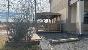 Un espacio de estar al aire libre con techo, baranda de madera, una planta en maceta y un edificio al fondo.