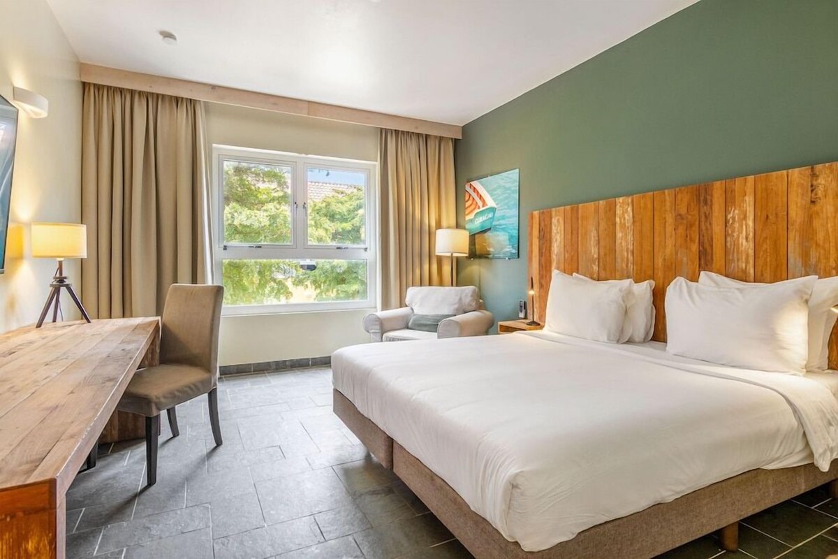 A hotel room with a large bed, a desk, a chair, and a window with curtains.