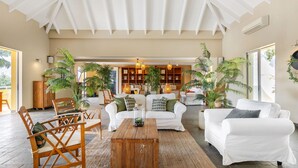 A spacious living area with a high ceiling, white sofas, wooden chairs, and a central coffee table. - Bayside Boutique Hotel - Blue Bay Golf & Beach Resort (Sint Michiel)