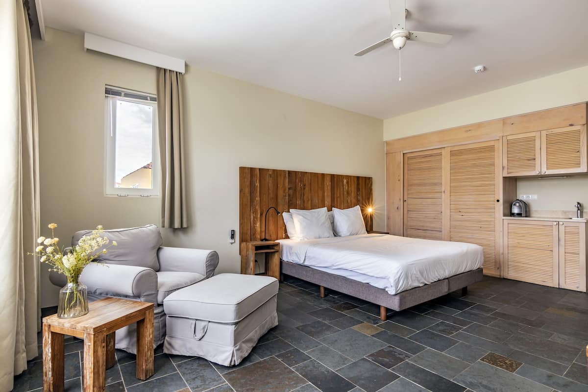 A bedroom with a bed, a sofa, a small table with a vase, a wooden headboard, a ceiling fan, and a wardrobe.