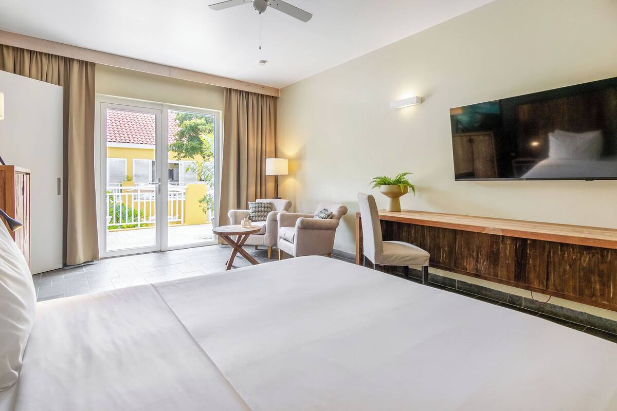 Una habitación de hotel con una cama grande, un escritorio con silla, un televisor montado en la pared y un ventanal corredizo que da a un espacio al aire libre.