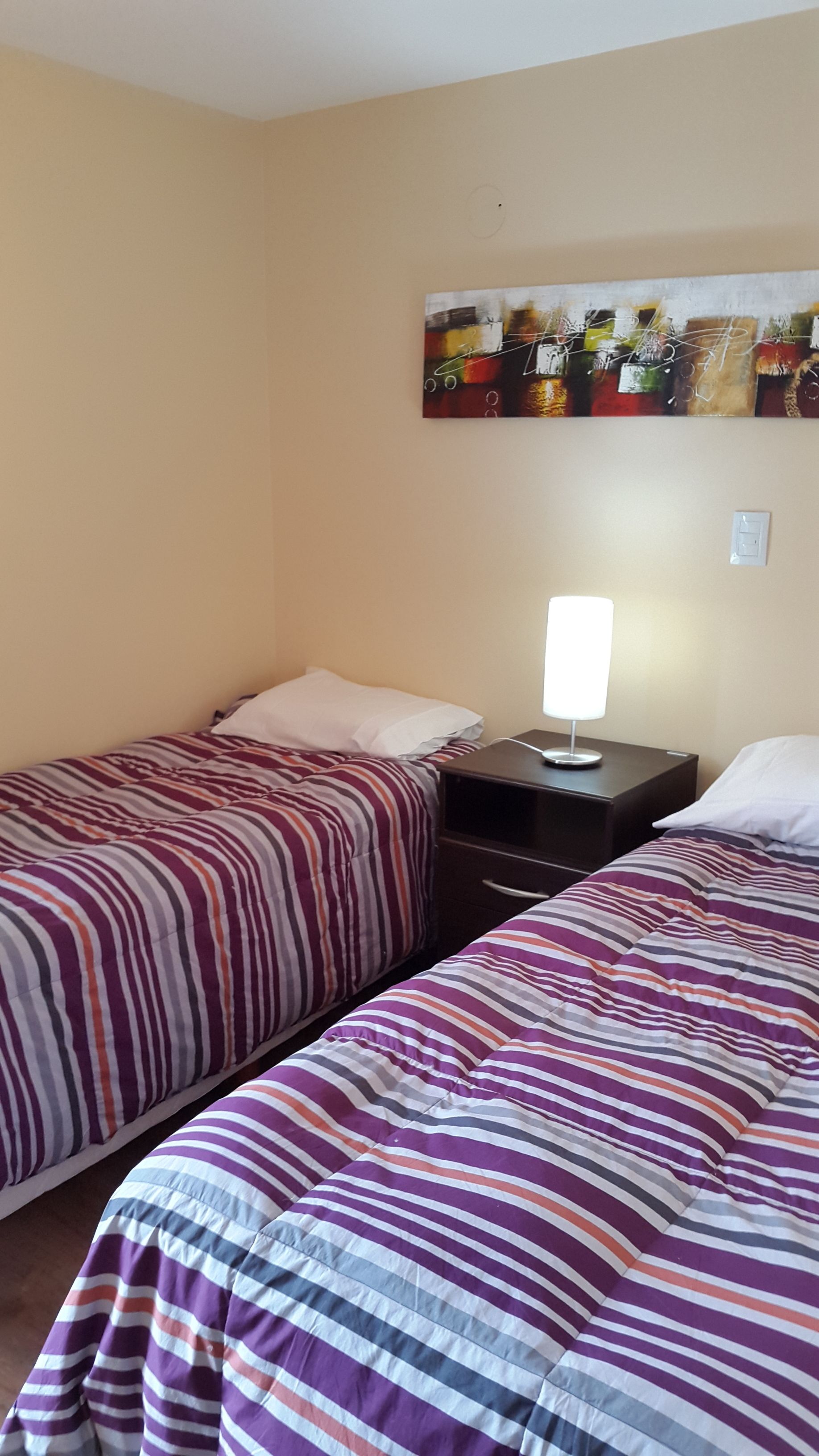 Une chambre avec deux lits, chacun agrémenté de draps à rayures, une table de chevet avec une lampe et un tableau au mur.