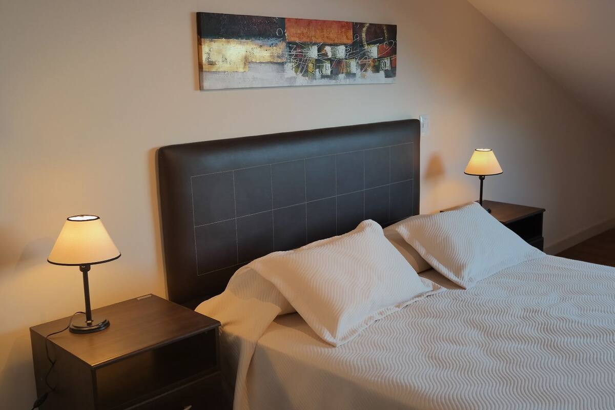 Un lit bien fait, avec une tête de lit, deux lampes de chevet et un tableau accroché au mur.