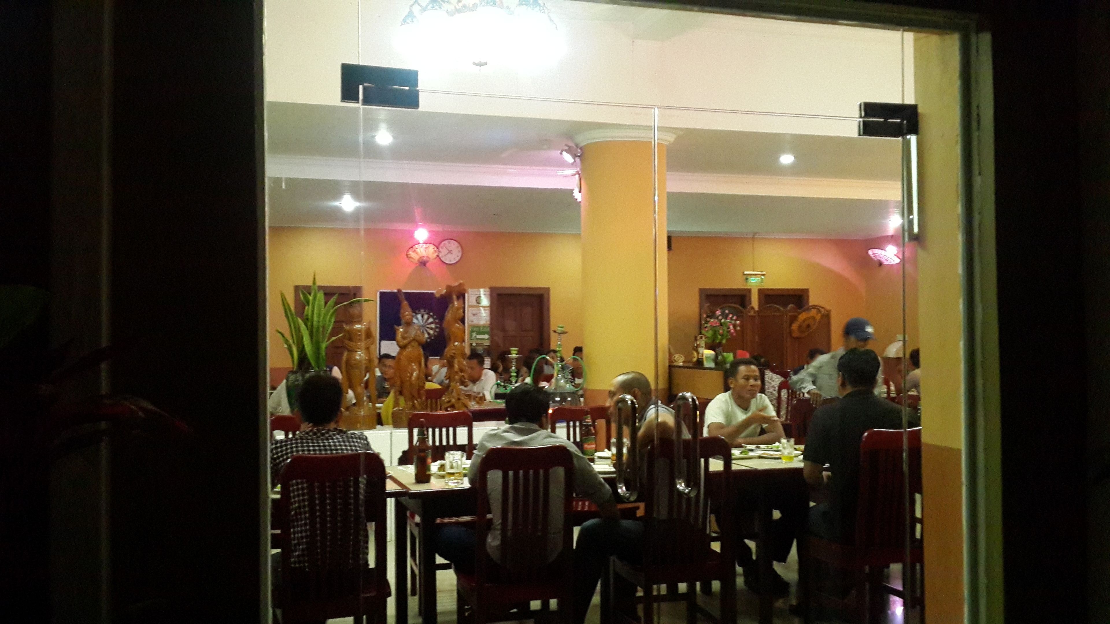 Un restaurante con varias mesas y sillas, un reloj en la pared y una planta en la esquina.