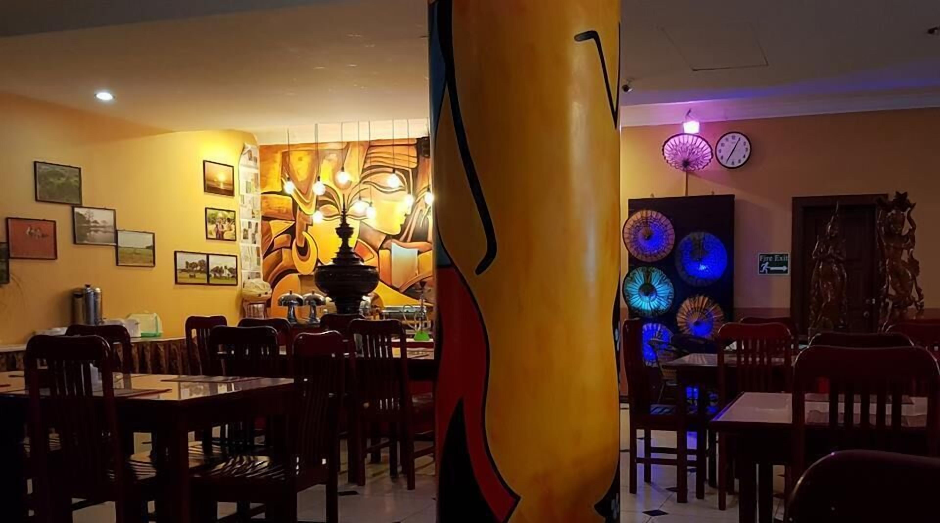 A restaurant interior with wooden tables and chairs, a large decorative wall with a central light fixture, and a wall-mounted clock.