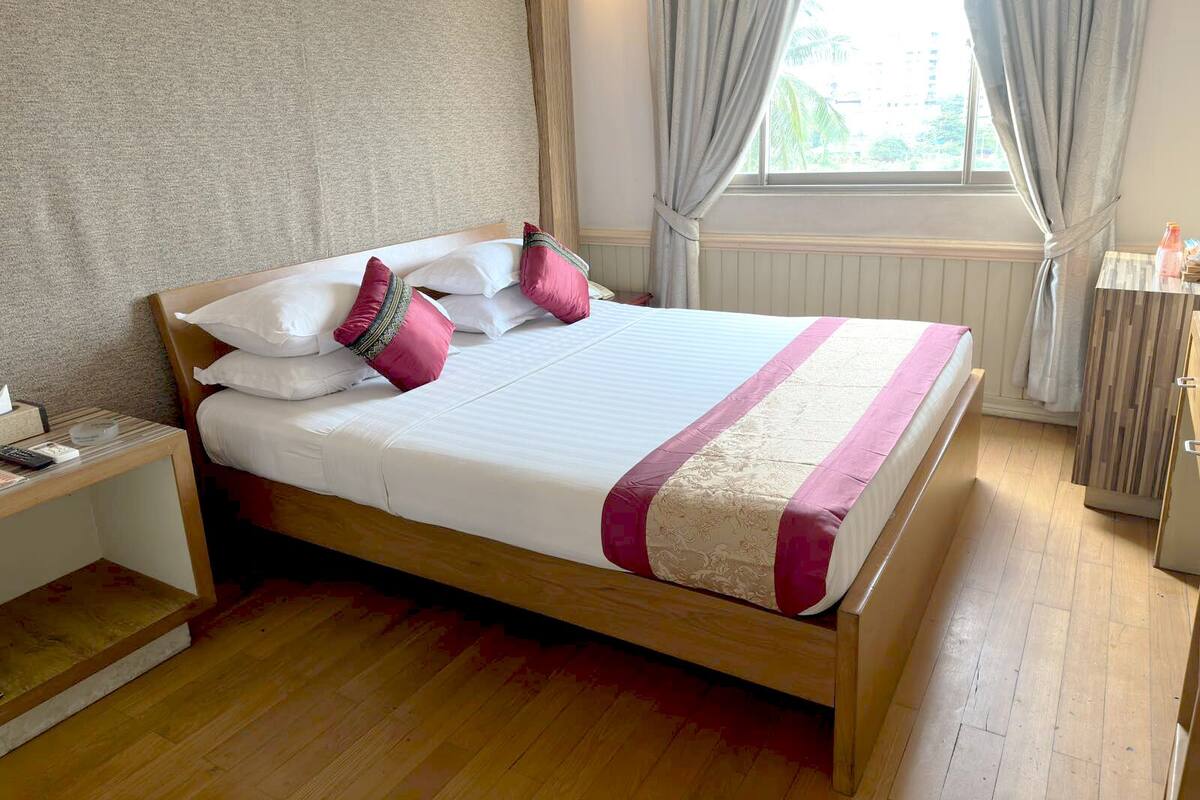 Ein ordentlich bezogenes Bett mit weißer und rosa Bettwäsche, ein Holz-Kopfbrett und ein Nachttisch mit Lampe.