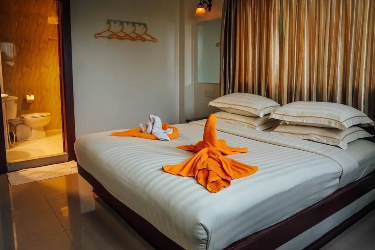 Ein Hotelzimmer mit Bett, Kissen, einem Badezimmer inklusive Toilette und Waschbecken sowie einem Spiegel.
