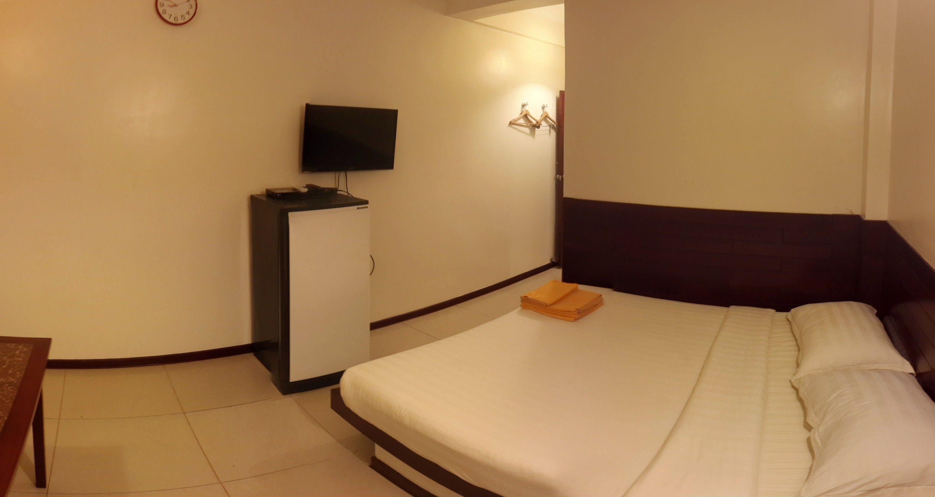 Una habitación de hotel con una cama, un televisor en un mueble y un reloj en la pared.