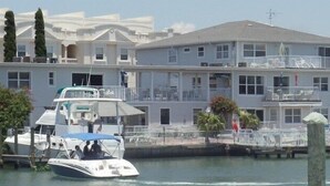 Een pand aan het water met een groot gebouw, balkon, een steiger met een boot en een rieten constructie.