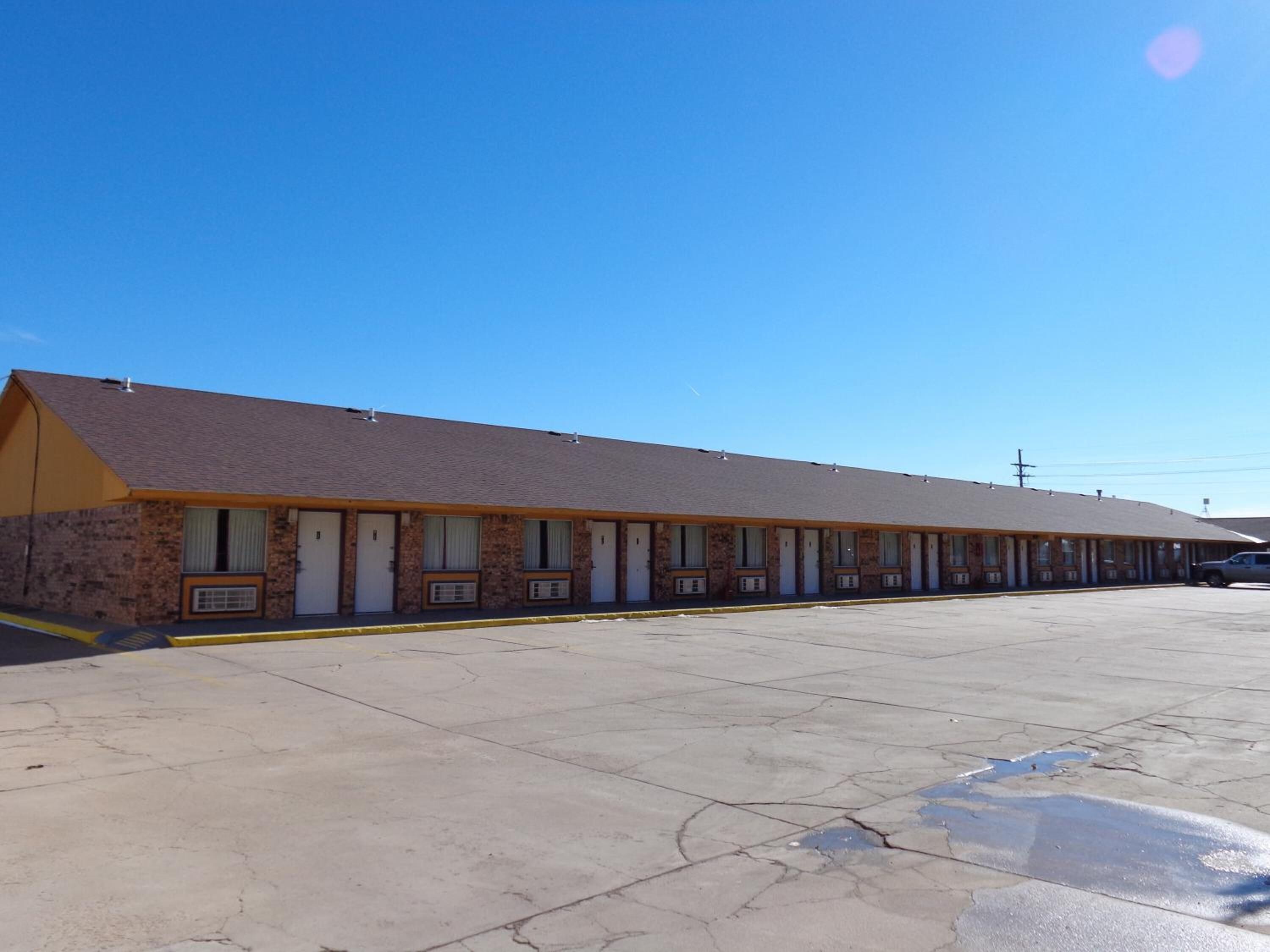 Un motel avec une rangée de chambres, un parking et un ciel bleu dégagé.