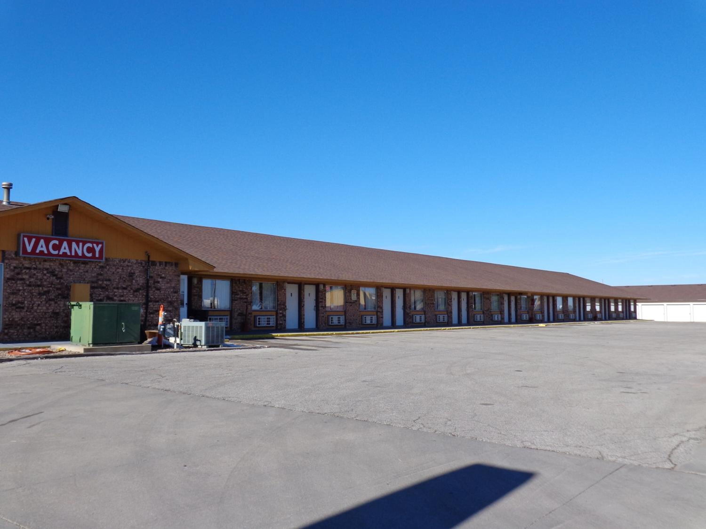 A large, single-story motel with a 'VACANCY' sign, a parking lot, and a clear blue sky.