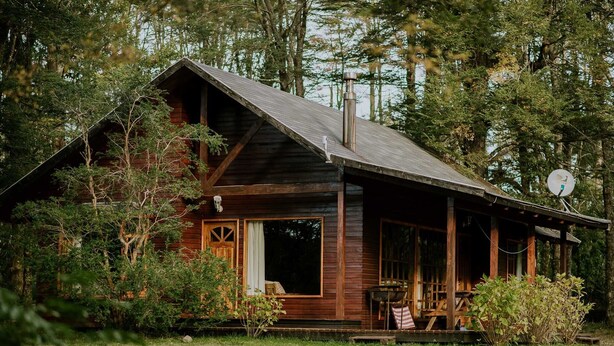 A rustic cabin with a porch, surrounded by dense forest. - Cabañas Metreñehue (Pucón)