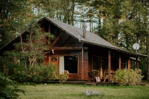 A rustic cabin with a porch, surrounded by dense forest. - Cabañas Metreñehue (Pucón)