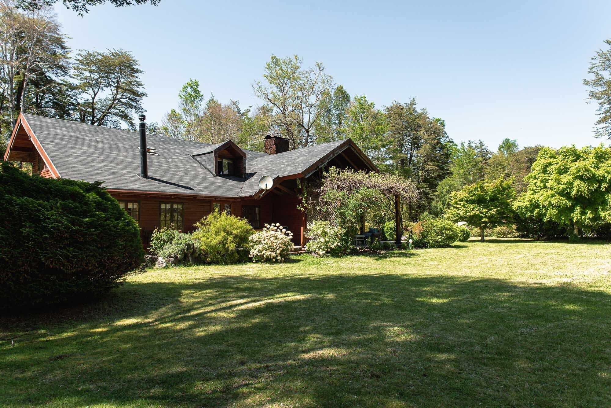 A log cabin with a sloped roof, surrounded by a well-maintained lawn and various trees.