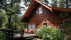 A wooden cabin with a deck, a covered porch, and a garden with hydrangea bushes. - Cabañas Metreñehue (Pucón)