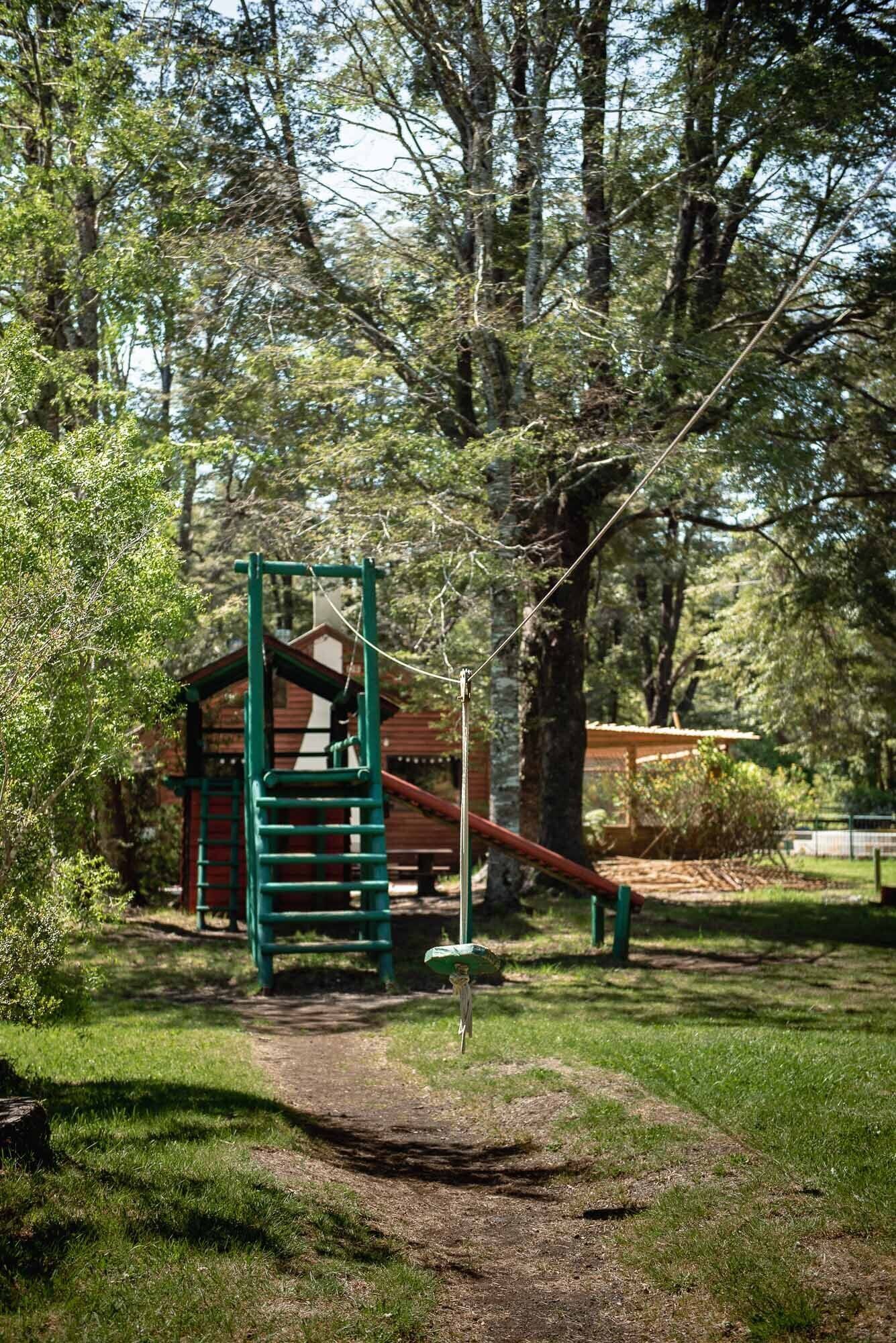 A playground with a climbing structure and a slide, surrounded by trees and grass.