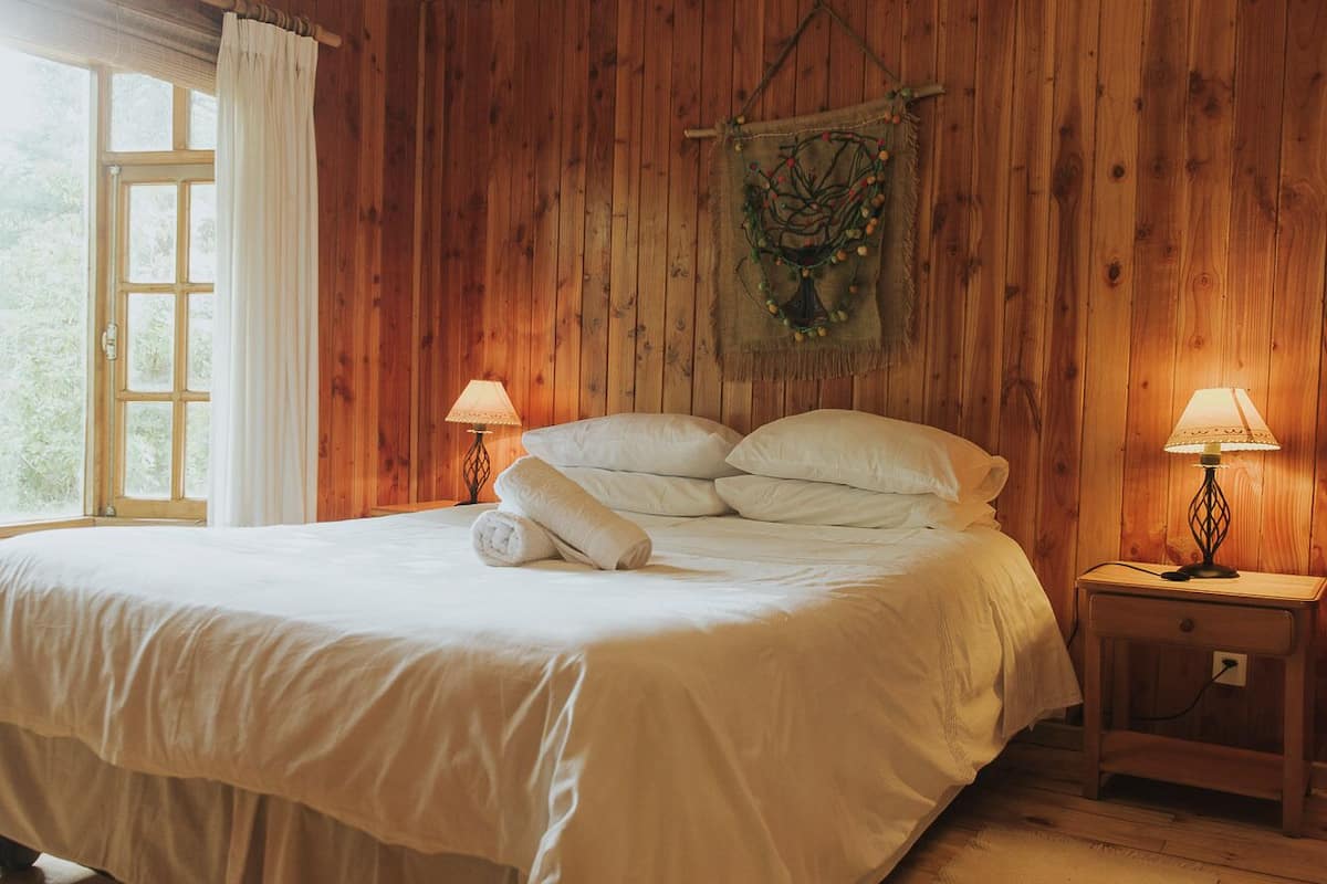 A wooden-paneled bedroom with a large bed, two bedside lamps, and a window with curtains.