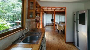 A kitchen with wooden flooring, a stainless steel sink, a refrigerator, and a dining area with a table and chairs. - Cabañas Metreñehue (Pucón)