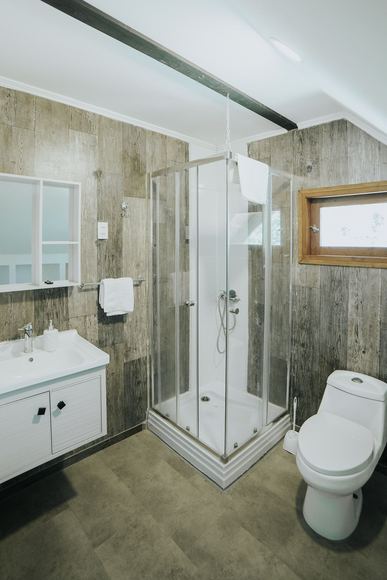 Un baño moderno con ducha de vidrio, lavamanos blanco con espejo arriba y un inodoro.