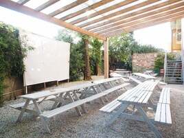 Patio esterno con tavoli da picnic in legno e zona coperta con tetto in legno.