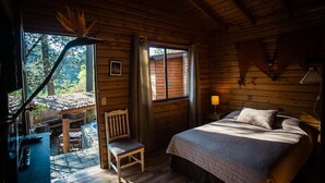 A cozy wooden cabin room with a bed, a chair, a table, and a window.