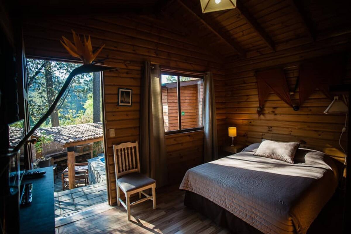 Acogedora habitación de cabaña de madera con cama, una silla, una mesa y un ventanal.