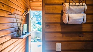 A wooden cabin interior with a shelf holding a vase and a small plant, and a towel rack with two towels.