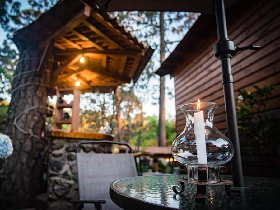 A glass table with a candle, a chair, and a stone wall in the background.