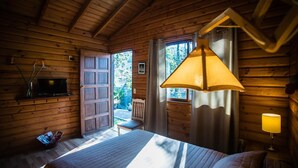 A wooden cabin bedroom with a bed, a television, and a window with curtains.