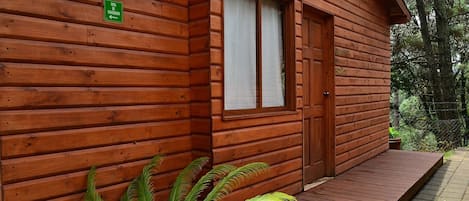 Una cabaña de madera con puerta y ventanas, un pequeño porche y un letrero que indica un baño.
