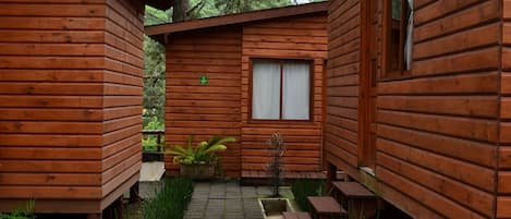 A wooden cabin with a small garden area, a window with curtains, and a bench.