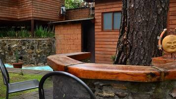 Una cabaña de madera con un muro de piedra, un banco y un árbol.