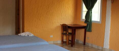 A room with two beds, a wooden table, a chair, a television, and a window with curtains.