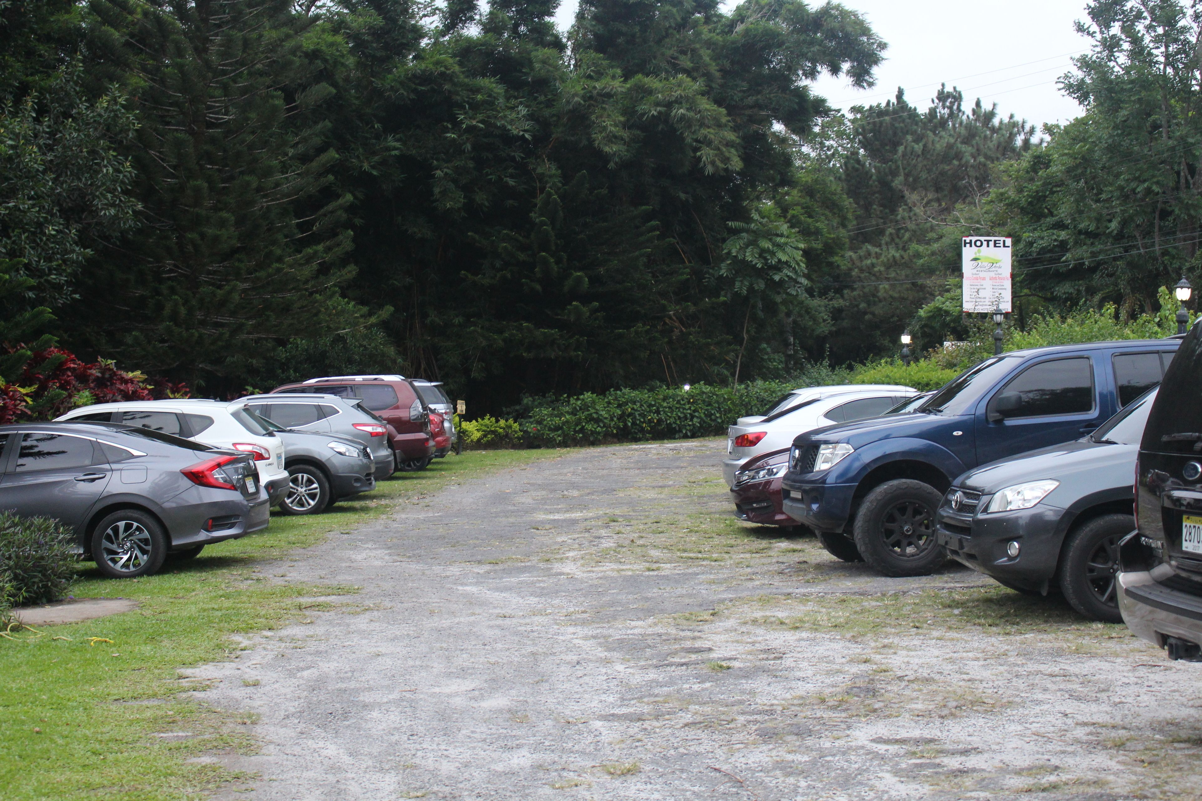 Ein Parkplatz mit mehreren parkenden Autos, einem Schild, das ein Hotel anzeigt, und einem Weg, der durch den Parkplatz führt.