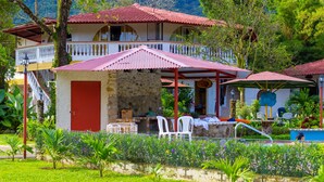 A two-story building with a red door, a stone wall, and a covered patio area with white chairs. - Hotel y Restaurante Valle Verde (El Valle de Anton)
