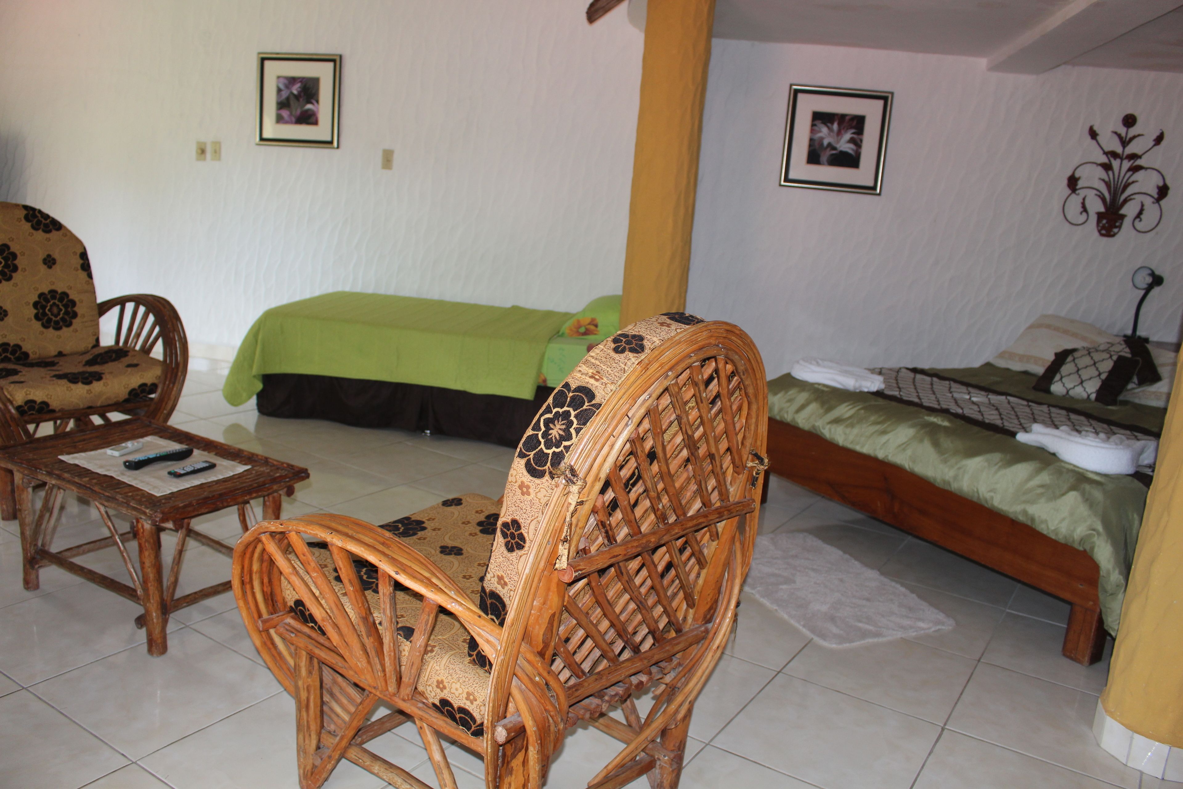 Una habitación con una cama, dos sillas, una mesita y una lámpara en la pared.