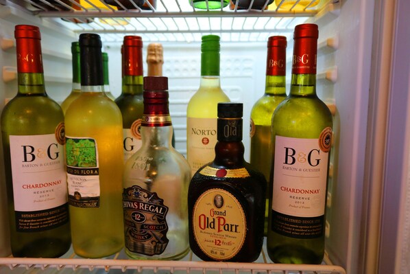 Un refrigerador lleno de diversas botellas de vino y licores, incluyendo marcas como B&G, Chivas Regal y Grand Old Parr.